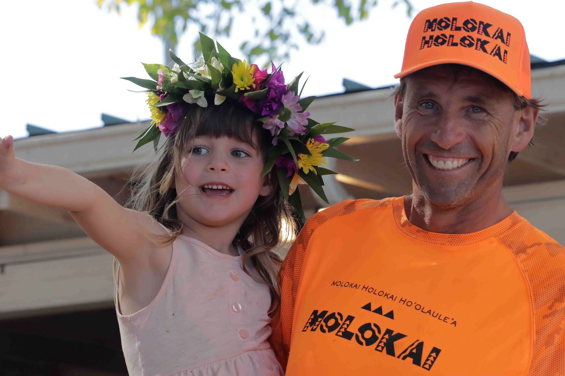 A little girl in a flower haku lei hugs her dad