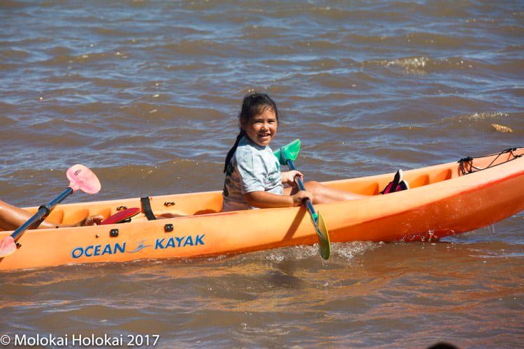 A young girl paddles an orange kayak