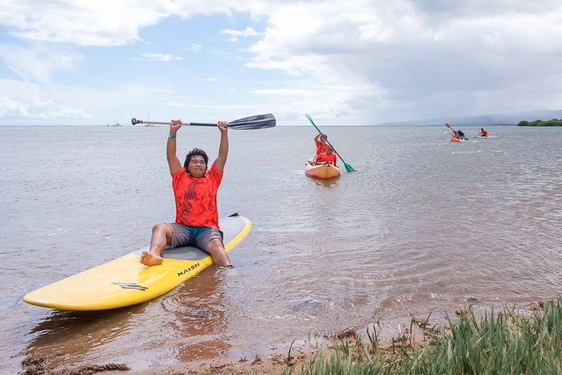 A keiki raises his paddle overhead on a stand-up paddleboard